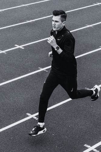 Jakob Ingebrigtsen running on a track wearing a black outfit with Nike logo and a PACE running watch from COROS