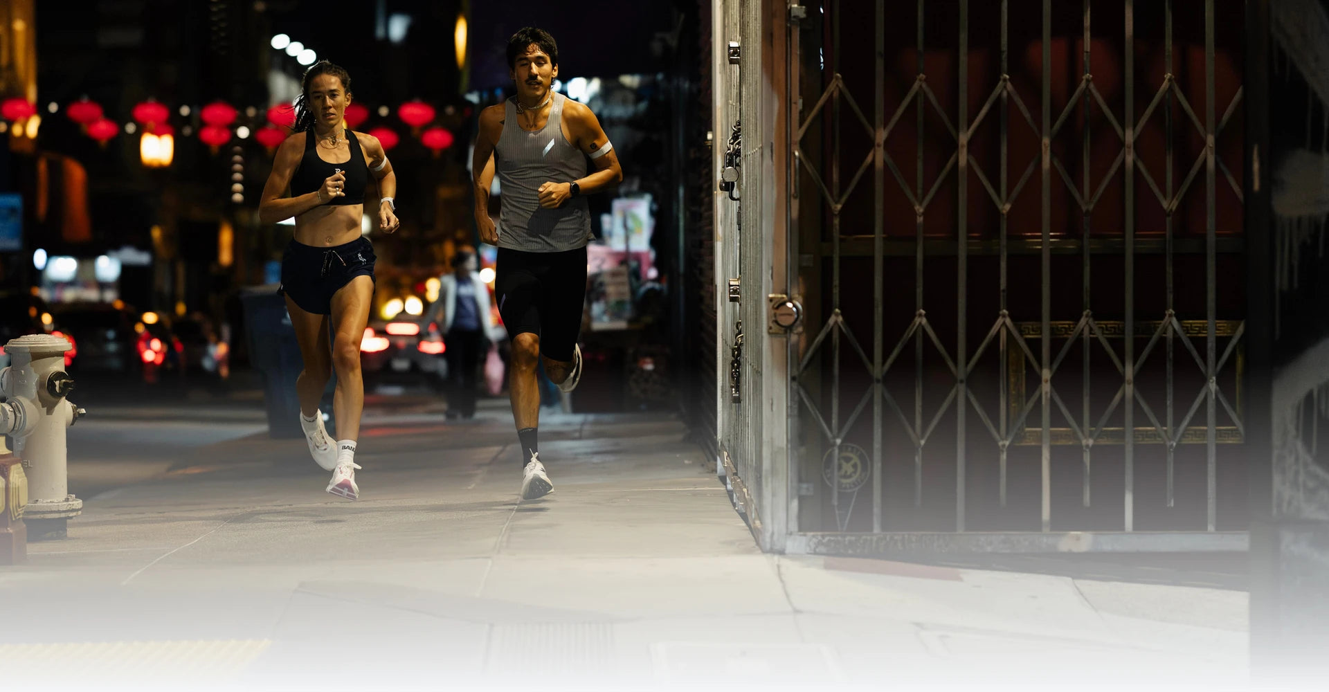 Two runners with running watches on a city street at night.