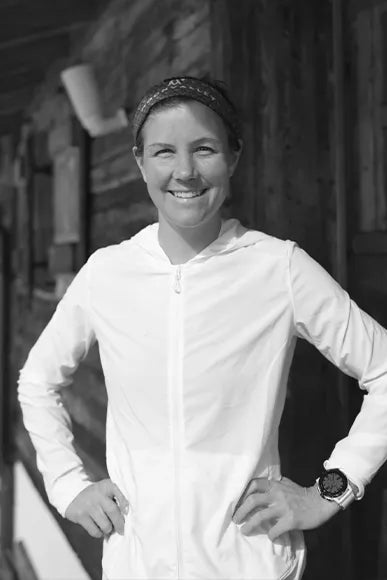 Emelie Forsberg standing up with white clothes on a dark background. Her COROS APEX smartwatch for trail and mountain running on her wrist.
