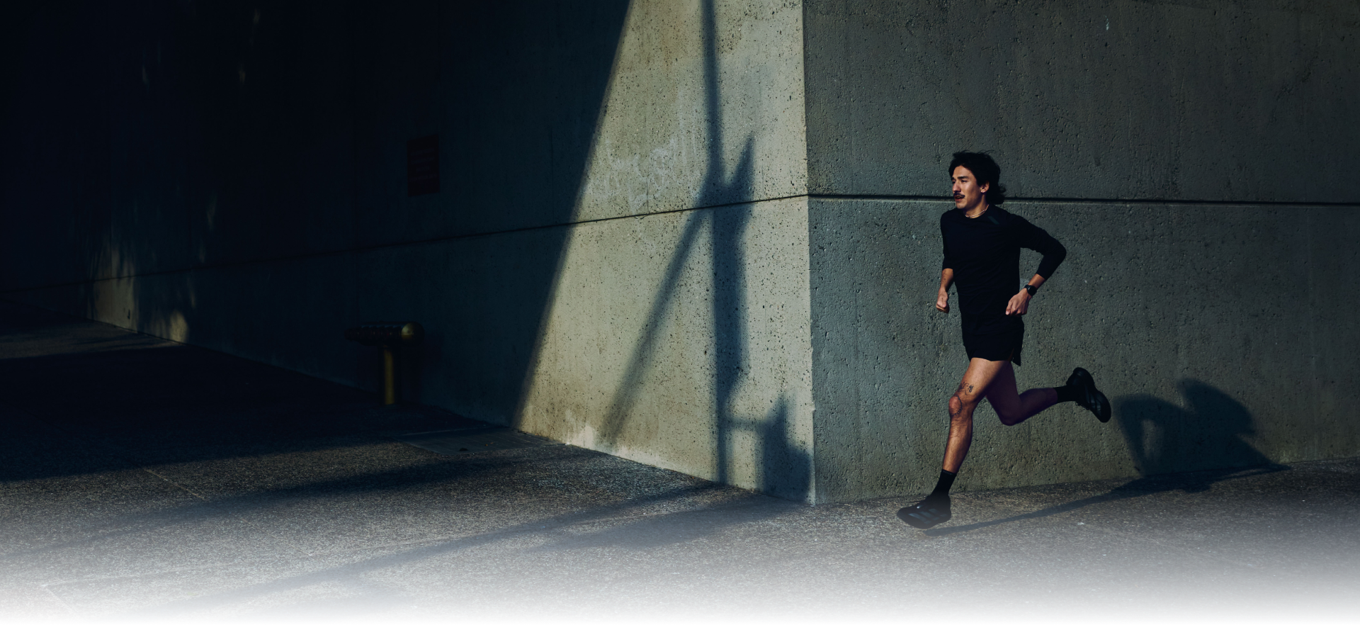 Man running in a tunnel with a strong light source casting a long shadow