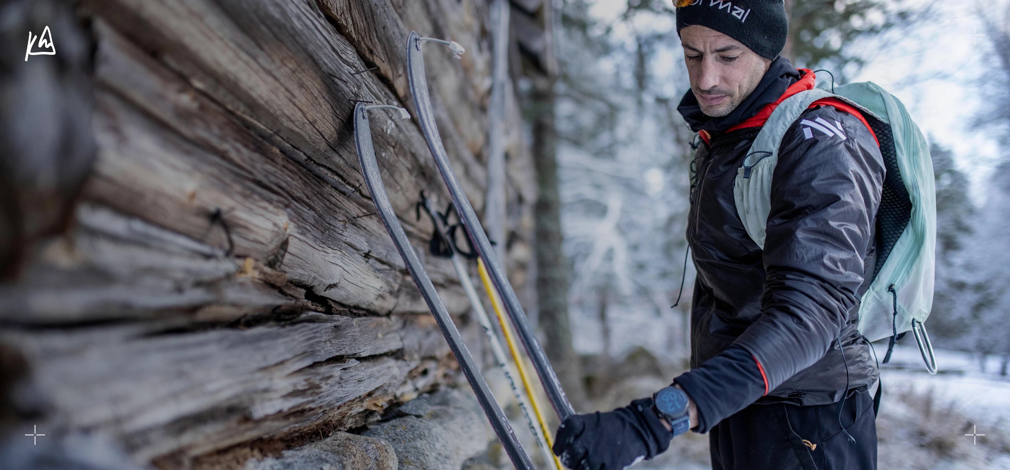 Kilian Jornet with skis and backpack near a wooden structure in a snowy landscape

